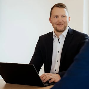 Einzelne Person arbeitet am Laptop und blickt Richtung Kamera