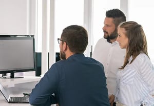 Drei Personen stehen gemeinsam vor einem Monitor im Büro und besprechen Eticor Aufgaben.