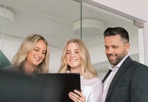 Drei Personen stehen zusammen im Büro und informieren sich über ISO Compliance Aufgaben auf einem Tablet.