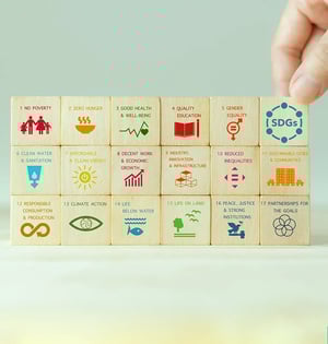 Hand stapelt Holzklötze mit Symbolen und Zielen der 17 UN-Nachhaltigkeitsziele (SDGs).